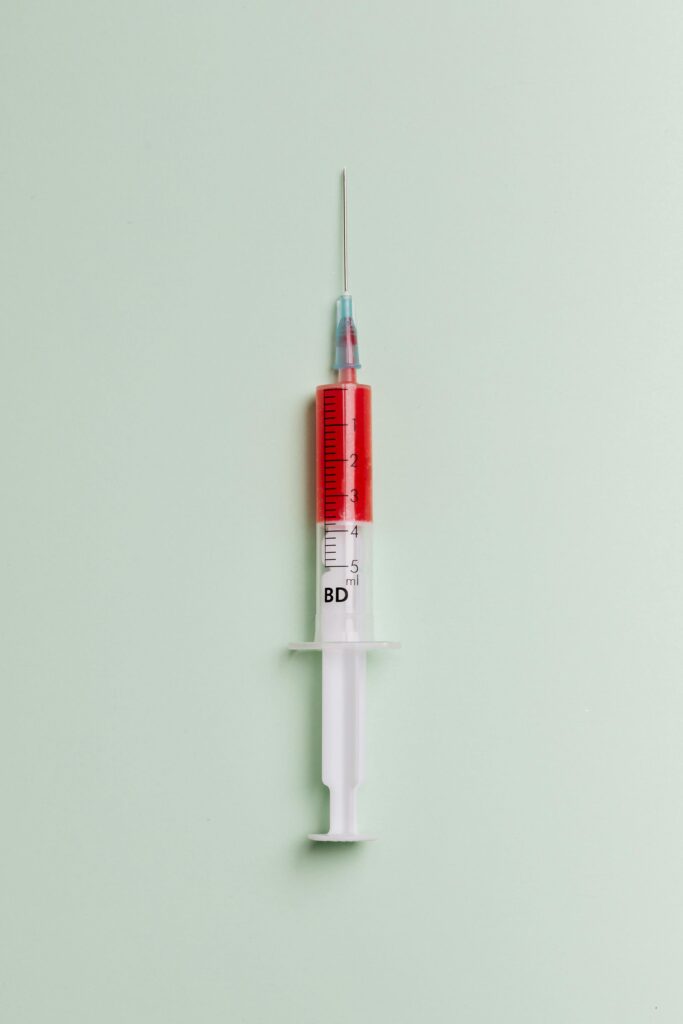 High-quality close-up of a syringe filled with red liquid on a light background.