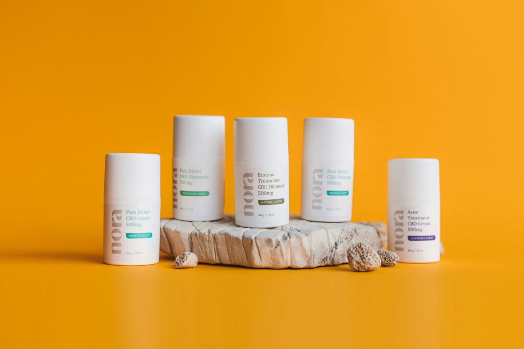 Five CBD cream products displayed on a yellow background with stones.