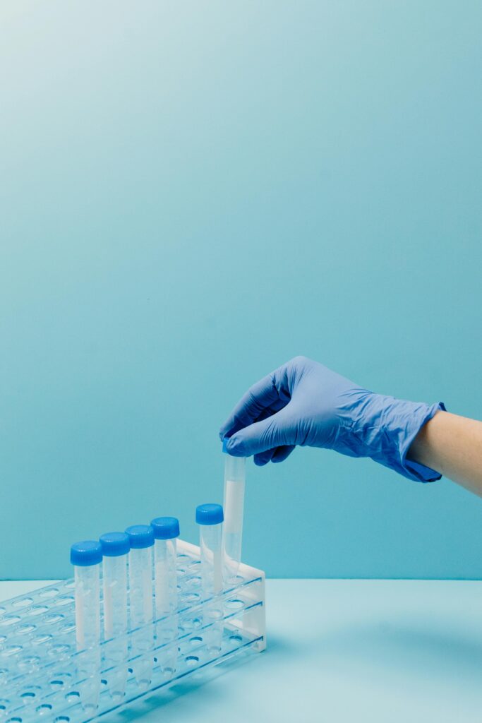 A gloved hand picking up a test tube from a rack in a laboratory setting.