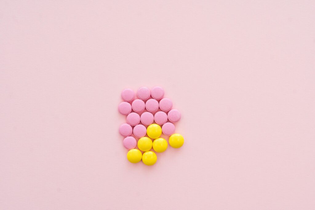 Pink and yellow pills arranged on a pastel pink background in a flat lay style.